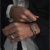 Hombre con blazer y camisa blanca luciendo la pulsera helicoidal, pulsera Enlazada y el anillo Corazón de Acero de Valurys, todos en acero quirúrgico.